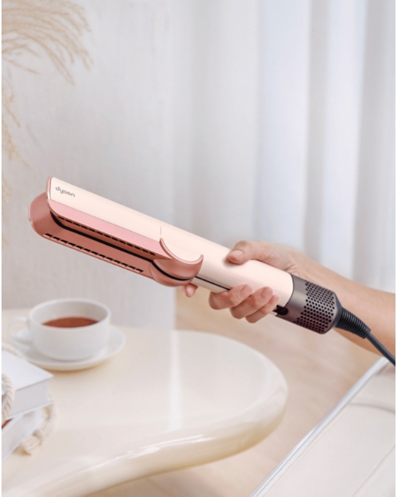 Dyson Airstrait straightener held in hand on a table.