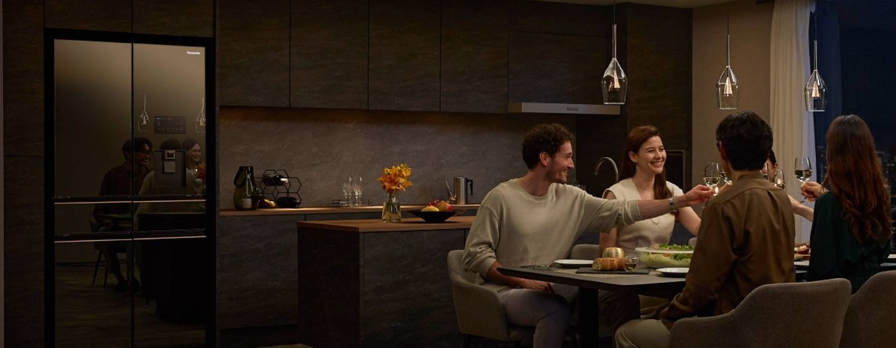 Group of friends dining in a modern kitchen with a Panasonic refrigerator in the background.