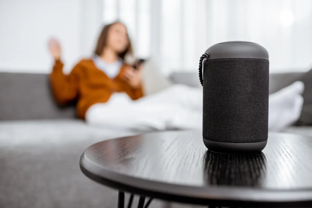 Wireless Speaker Malaysia guide. A woman relaxing at home with a portable wireless speaker on the table.